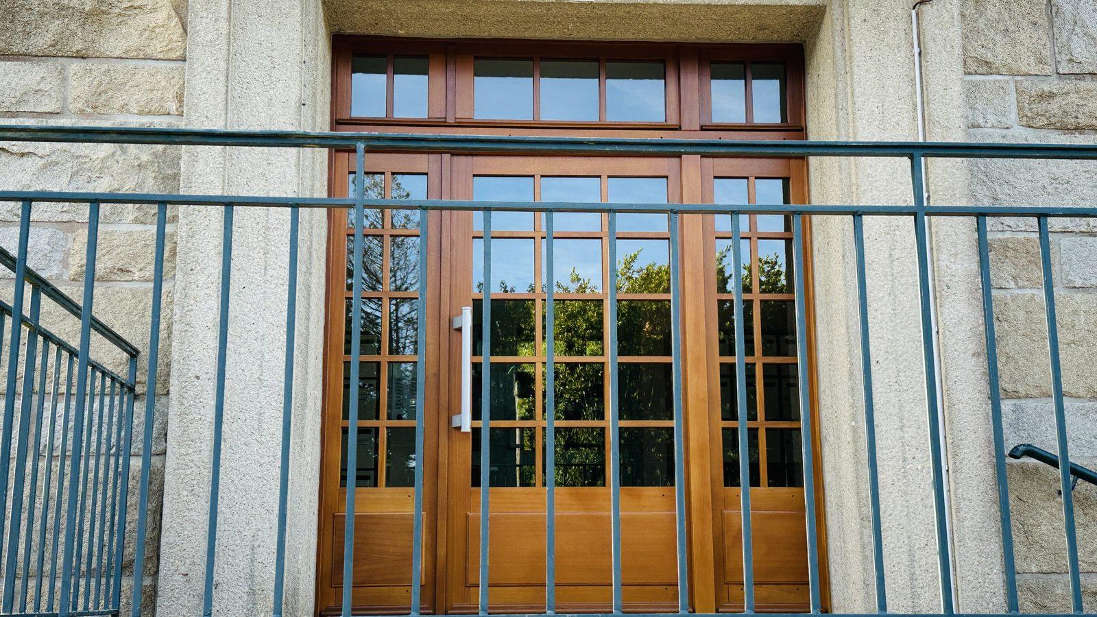 La porte d'entrée de l'immeuble : une porte de bois vitrée dans une façade de granit, derrière une grille de fer.